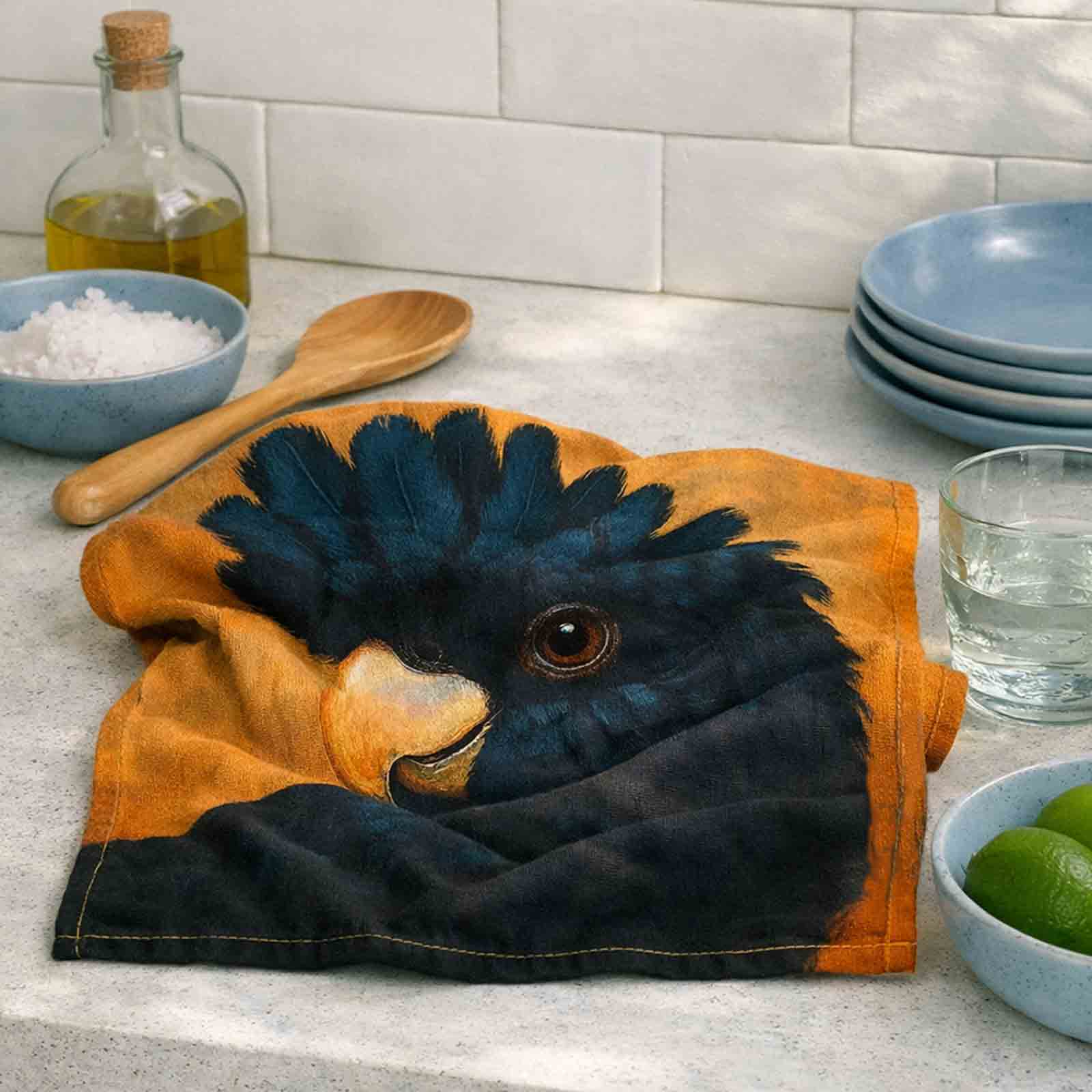 Black Cockatoo cotton tea towel styled on a coastal kitchen bench with natural folds, premium cotton texture