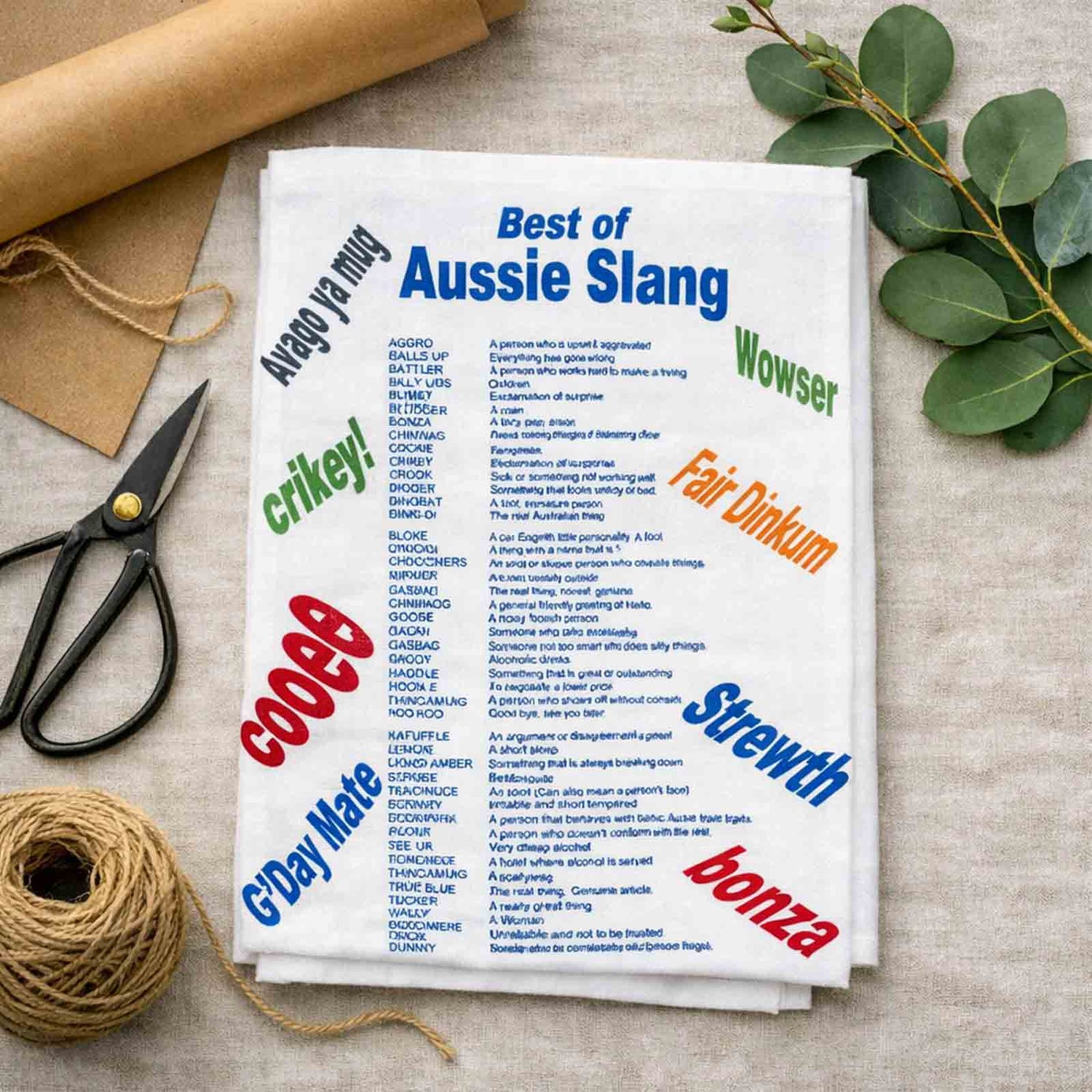 Tea towel with Australian slang words on a table with scissors and twine.