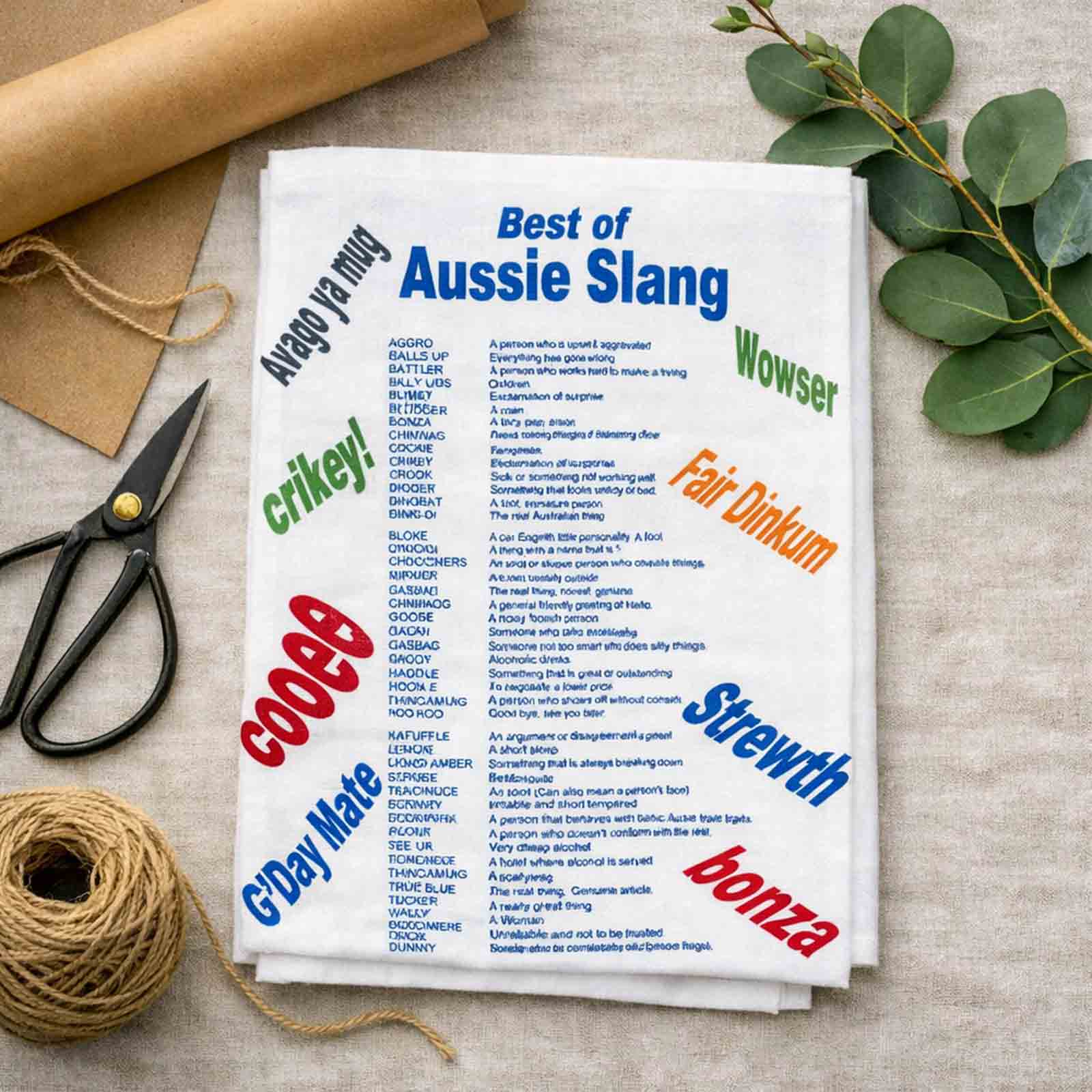 Tea towel with Australian slang words on a table with scissors and twine.