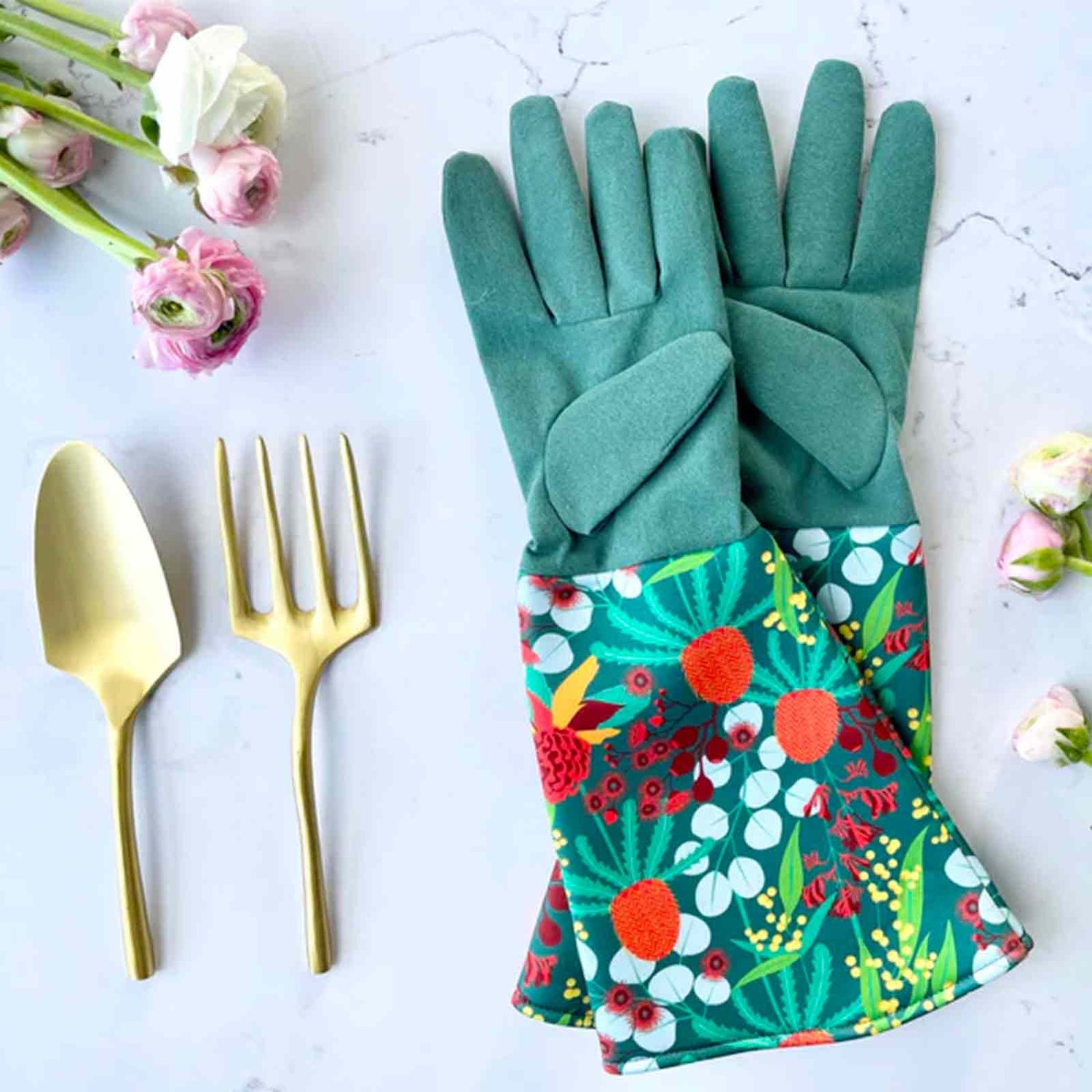 Gardening gloves with colorful Australian Botanicals pattern, gold spoon, and fork on a light background