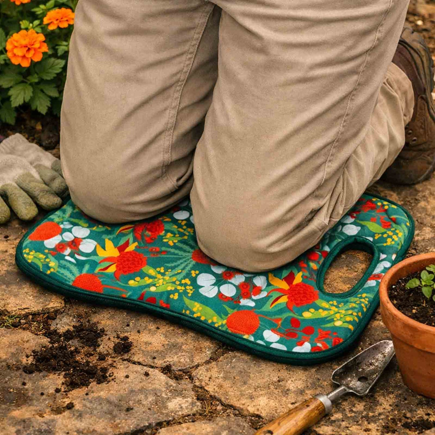 Person kneeling on a colorful Australian Botanicals garden mat with gardening tools and plants around.