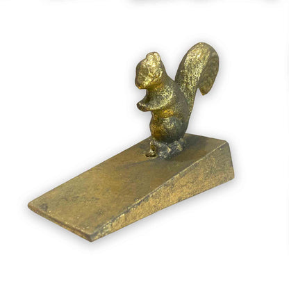 Gold coloured metal squirrel door stop wedge on a white background