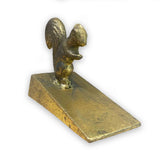 Gold coloured metal squirrel door stop wedge on a white background