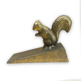 Gold coloured metal squirrel door stop wedge on a white background