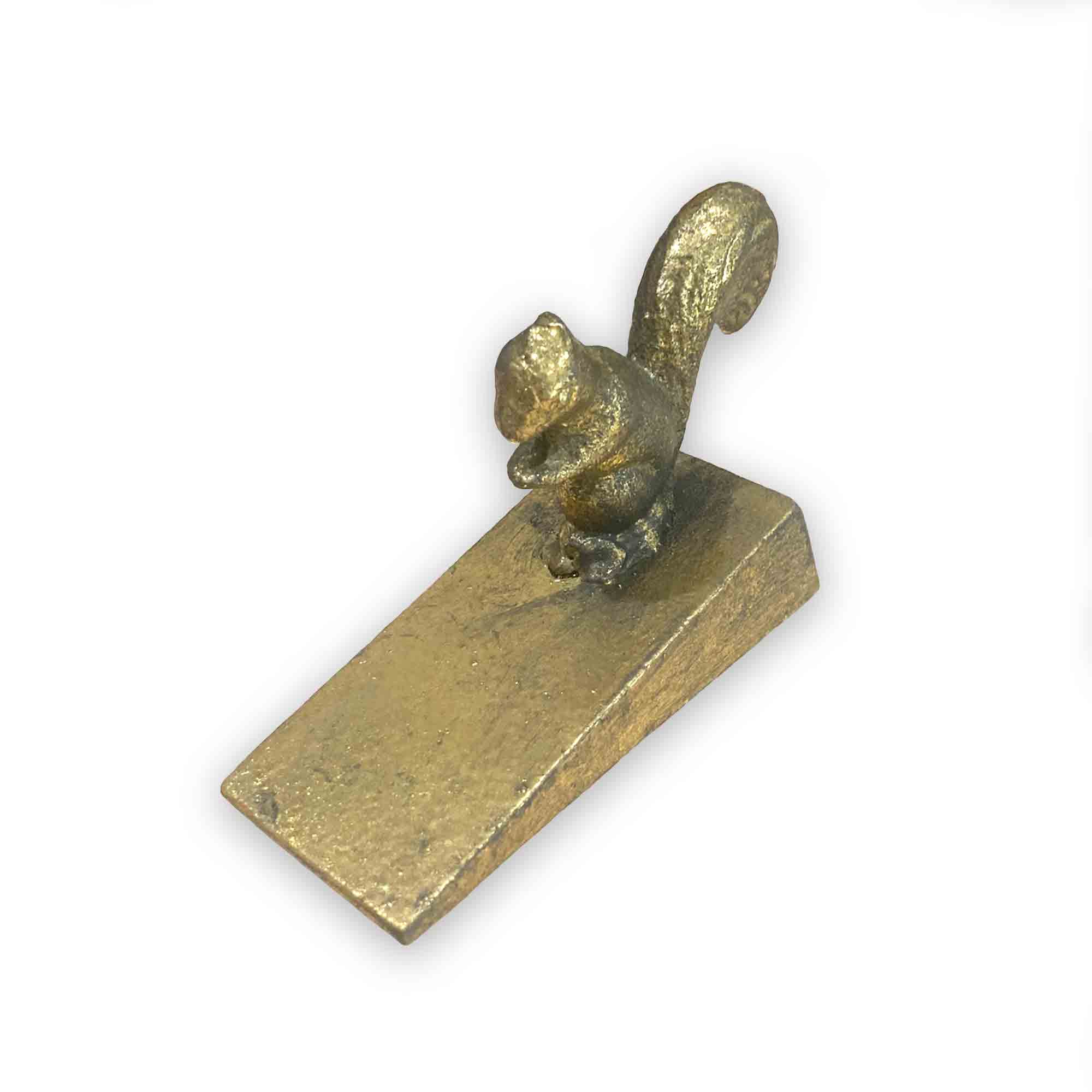 Gold coloured metal squirrel door stop wedge on a white background