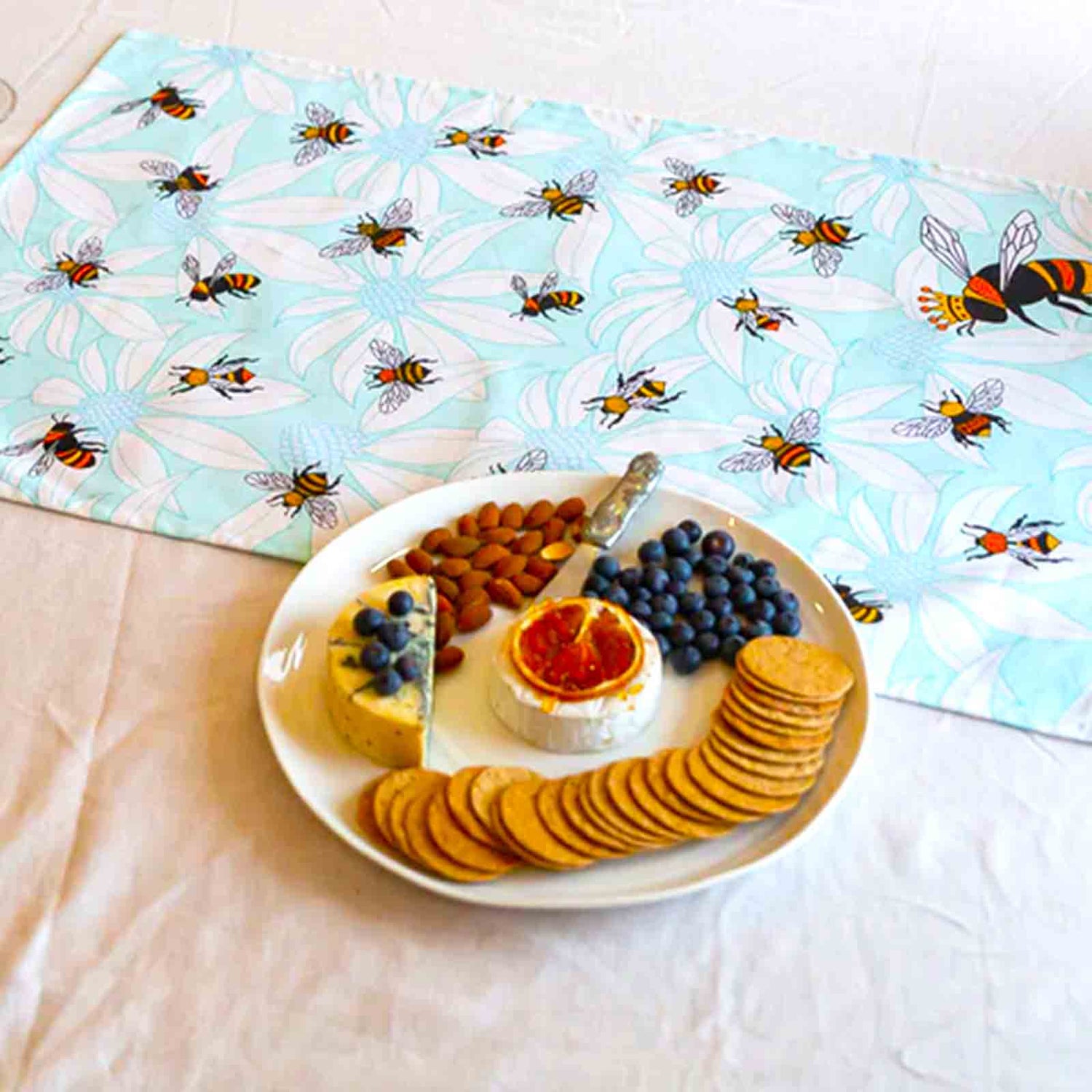 Platter of assorted snacks on a table with a bee-patterned tea towel.