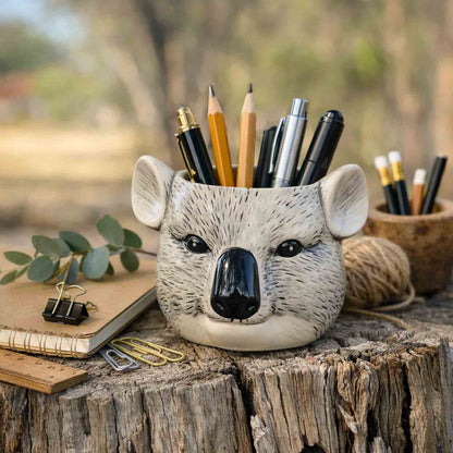 Koala-shaped pencil holder with stationery items on a wooden surface