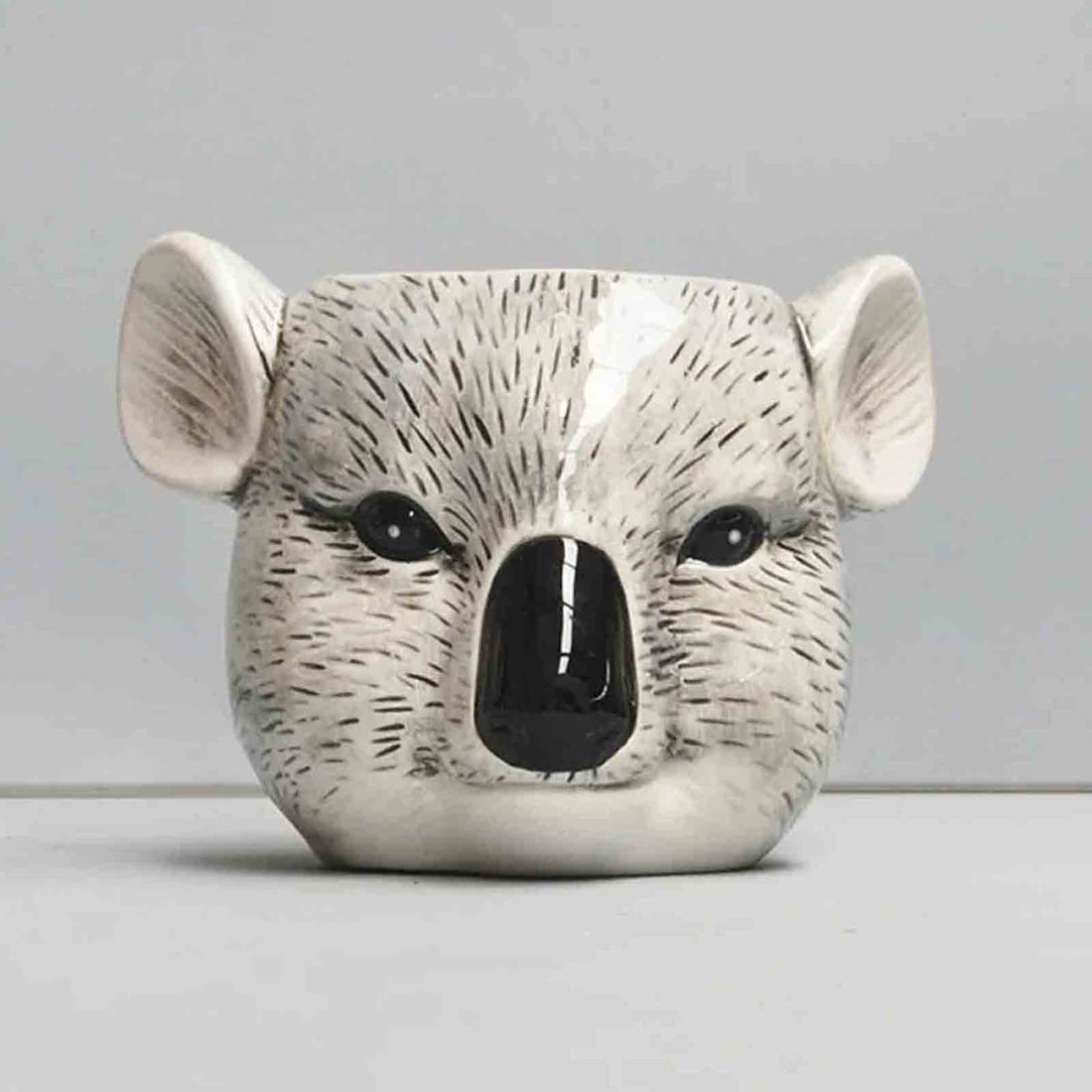 Ceramic pot shaped like a koala face on a plain background