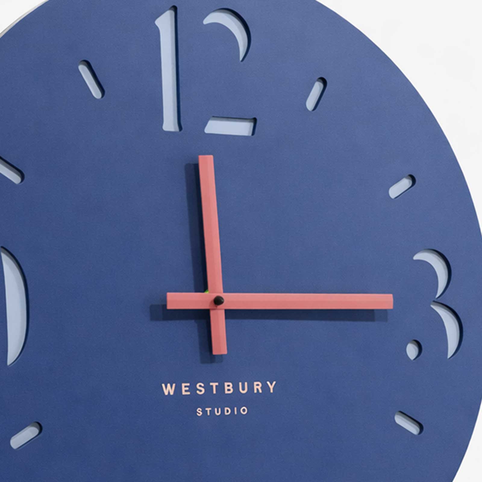 Close‑up of coral‑pink metal clock hands on deep blue wooden clock