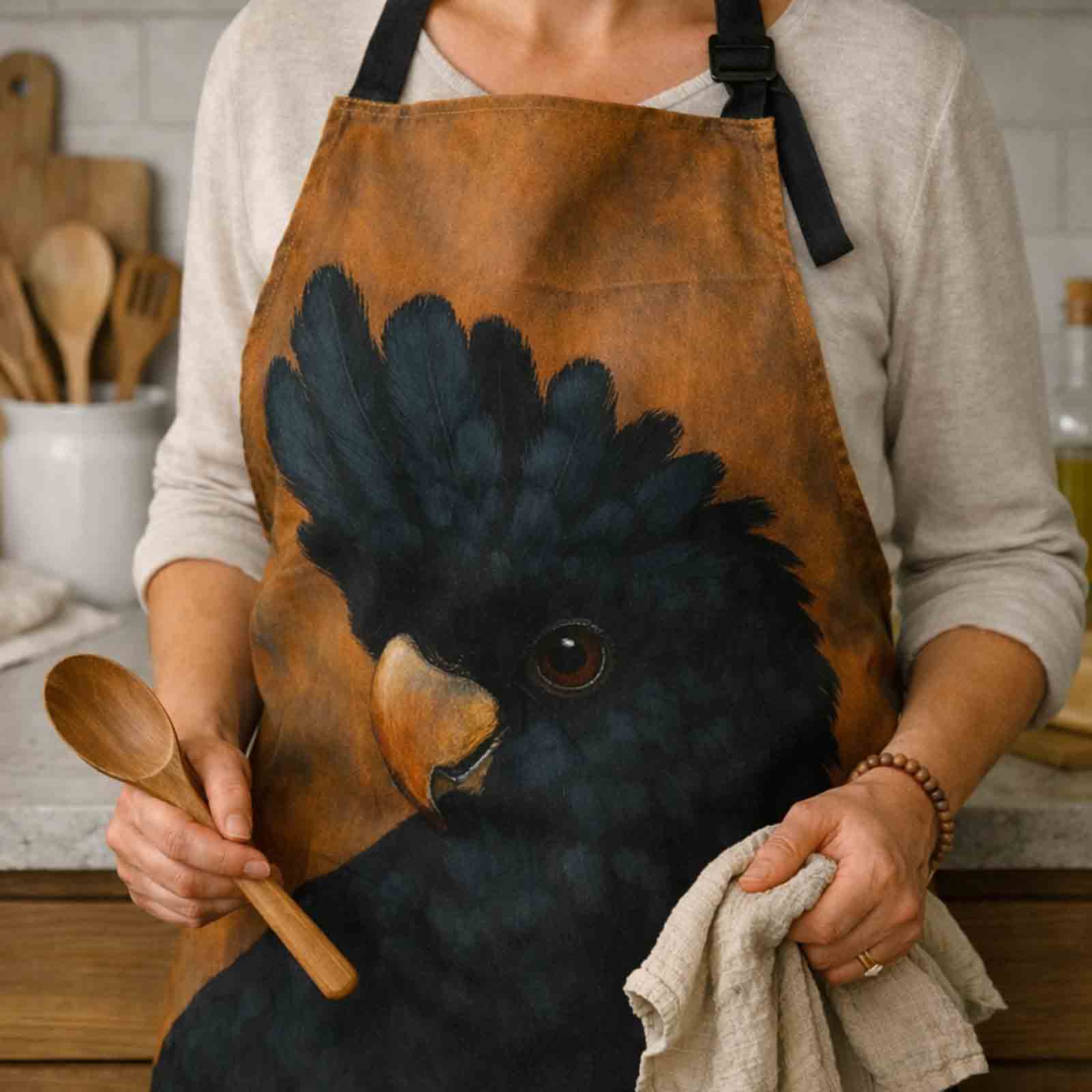Person wearing a brown apron with an Australian Black Cockatoo bird design in a kitchen setting