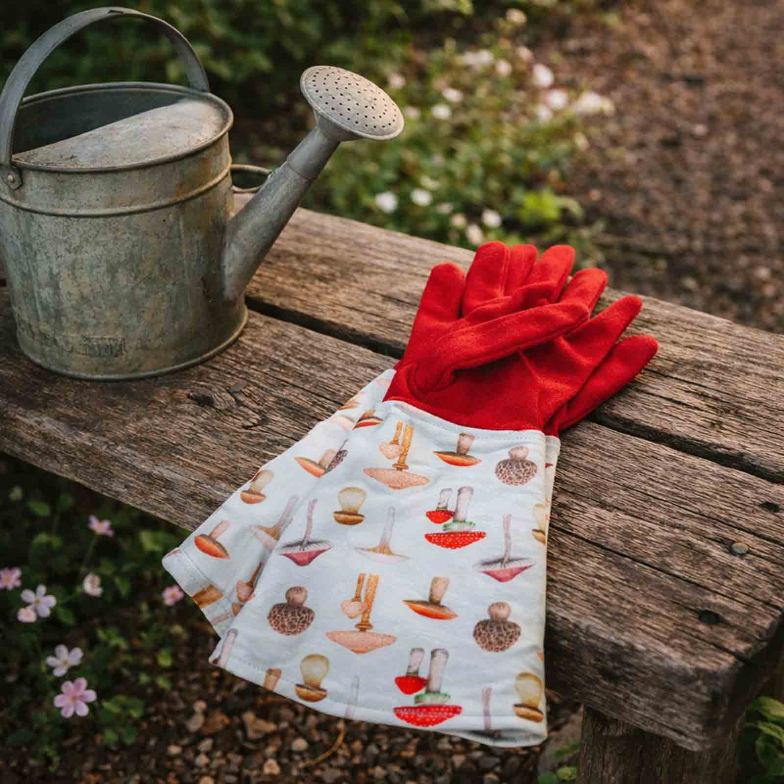 Mushroom patterned gardening gloves sitting on a wooden bench next to a rustic watering can
