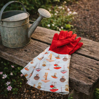 Mushroom patterned gardening gloves sitting on a wooden bench next to a rustic watering can
