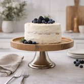 White cake with berries on a wooden cake stand in a kitchen setting