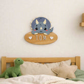 Customisable personalised dinosaur wooden door sign hanging on a wall above a bed with a dinosaur plush toy