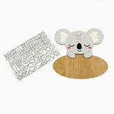 A wooden koala-themed name sign and matching alphabet sticker sheet on a plain white background. The koala is light gray with white ears, a black nose and mouth, pink cheeks, and sits on a round natural wood base.