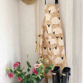 Warm greyish beige sheep‑print apron hanging on white wall, rustic farmhouse kitchen accessory - Hello Homewares.